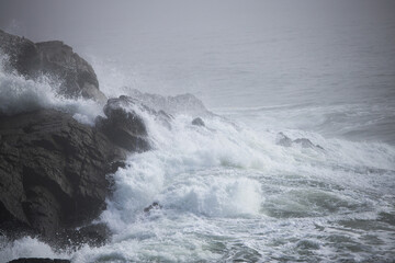 Ocean waves crashing onto a rocky shore on a foggy morning