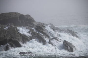Ocean waves crashing onto a rocky shore on a foggy morning