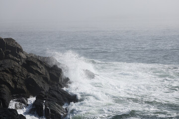 Ocean waves crashing onto a rocky shore on a foggy morning