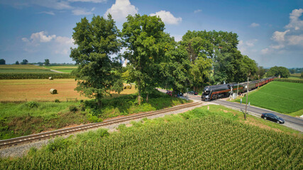Fototapeta na wymiar Drone View of an Antique Steam Engine, Approaching, Blowing Steam and Traveling Along the Countryside on a Sunny Day