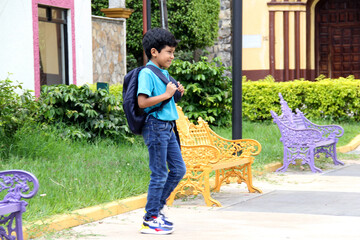 Poor dark-haired 8-year-old Latin boy walks down the street on his way to study back to school with a backpack, the family makes an economic effort in their poverty to buy the books and notebooks
