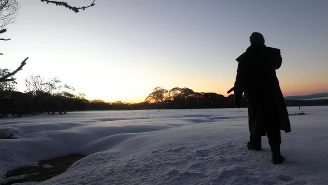 A bushman in a stockman jacket walks out accross the snow in the early morning sun in Victoria Australias high country.