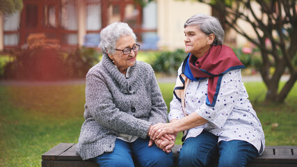 Two old women sitting on bench in park holding hands smiling happy life long friends enjoying...