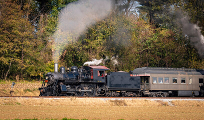 A View of a Restored Steam Passenger Train Blowing Smoke and Steam Traveling Along a Rural Countryside on a Sunny Day