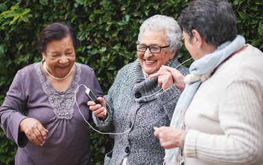 Happy old women listening to music on smartphone wearing earphones smiling enjoying fun celebrating retirement together outdoors