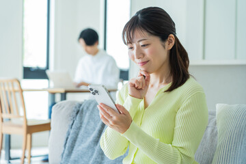 自宅のソファでくつろぎながら携帯を触る日本人女性