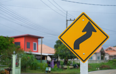 Yellow traffic sign with twisty arrow symbol at rural road Thailand to warn drivers be careful when driving on twisty way road after rain