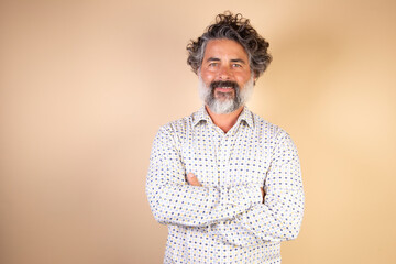 Successful middle-aged caucasian man dressed casually with arms crossed isolated on beige background