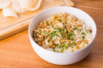 Close up view of Chicken congee or chicken porridge. Equipped with shredded chicken, cakwe or youtiao, garlic crackers, peanuts and spring onions