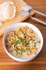 Close up view of Chicken congee or chicken porridge. Equipped with shredded chicken, cakwe or youtiao, garlic crackers, peanuts and spring onions