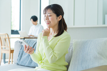 自宅のソファでくつろぎながら携帯を触る日本人女性