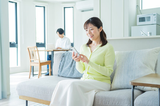 自宅のソファでくつろぎながら携帯を触る日本人女性