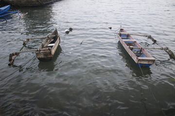 Two fishing boats, made of wooden planks, lean on the shore.