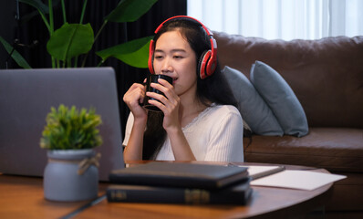 Happy young woman wearing wireless headphone reading online news on her laptop, sitting in living room.