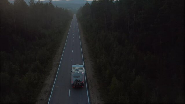 Drone follows rv camper from the back it sunset on road in wilderness