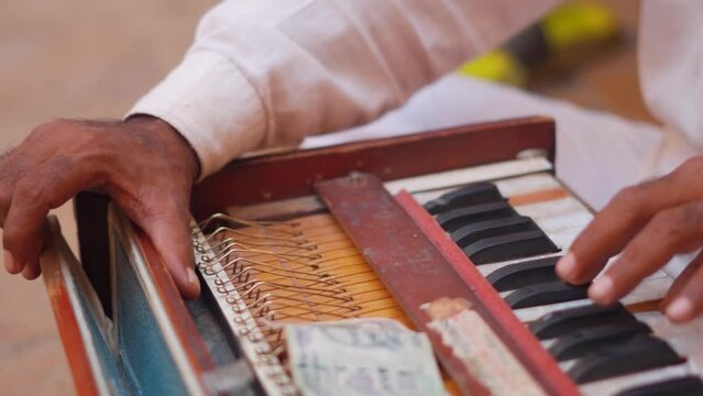 Closeup shot of hands of an Indian street performer playing Harmonium on the street at Jaisalmer in Rajasthan, India. Out of focus money on top of the Harmonium while man plays it. Indian culture. 