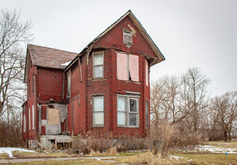 Old red brick abandoned boarded up house in Detroit Michigan on a cloudy day