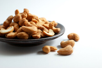 Salted cashew nuts on a black ceramic plate and placed on a white floor.