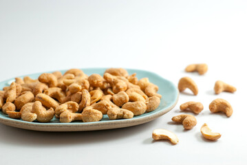 Salted cashew nuts on a ceramic plate and placed on a white floor.