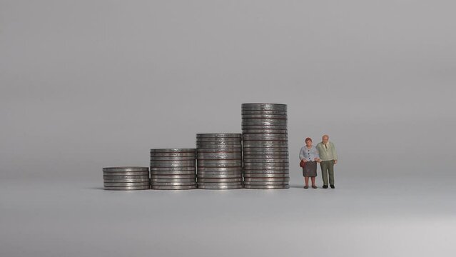 Miniature people and the concept of an aging society. A miniature old couple standing next to a pile of step coins.
