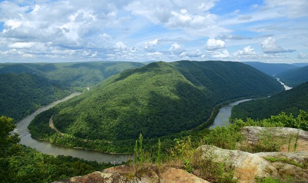 looking out at a horseshoe bend in the new river, railway,   and forested  hills in summer from the grandview main overlook in the new river gorge national park, west virginia