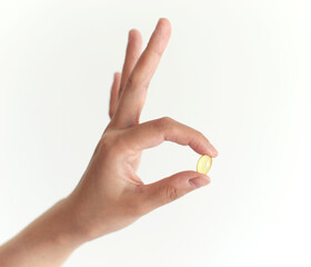 female hand holding a show clear yellow pill capsule on a white background