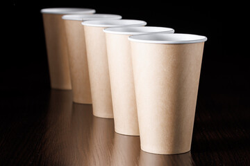 Several paper disposable eco-friendly cups stand in a row on a black background. Selective focus.