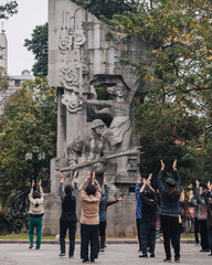 Hanoi, Vietnam - February 25th, 2022 : a group of women exercising in Hanoi in front of a war memorial statue