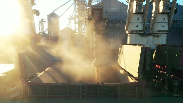 Aerial view fom above - wheat loading to bulker ship cargo hold at sea grain elevator in sea port. Wheat shipment from silo to vessel via moving trunk at a sea port terminal. Maritime transport.