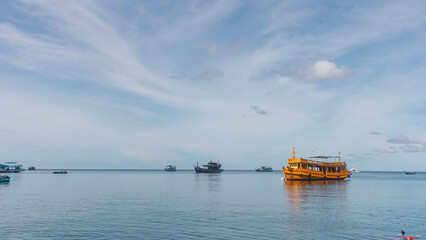Panorama of a yellow dive boat on the horizon with blue still waters and blue sky wallpaper, koh tao island, gulf of thailand
