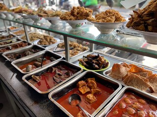 Padang food stalls share a variety of buffet menus with vegetables, chicken curry sauce, beef, eggs, tofu, tempeh. the waiter prepares the arrangement of the food. Menu in glass display case.