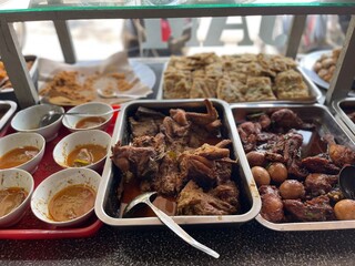 Padang food stalls share a variety of buffet menus with vegetables, chicken curry sauce, beef, eggs, tofu, tempeh. the waiter prepares the food. Menu in glass display case. Asia and asian food. Pile.
