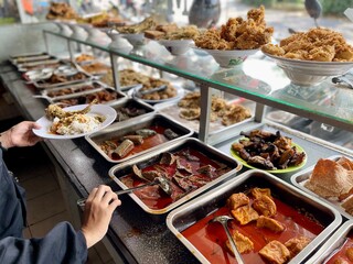 Fototapeta Padang food stalls share a variety of buffet menus with vegetables, chicken curry sauce, beef, eggs, tofu, tempeh. the waiter prepares the food. Menu in glass display case. Asia and asian food. Pile. obraz