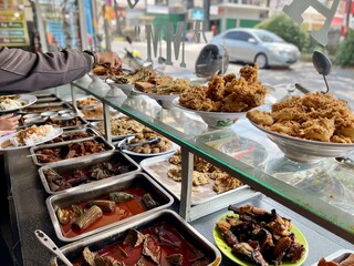 Padang food stalls share a variety of buffet menus with vegetables, chicken curry sauce, beef, eggs, tofu, tempeh. the waiter prepares the arrangement of the food. Menu in glass display case.