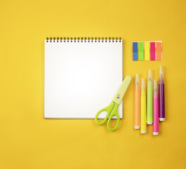 Notepad on a yellow background, colored markers and green scissors. 