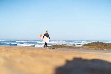 Fototapeta na wymiar Surfer woman at the beach walking with her surfboard in the morning. Female surfer woman