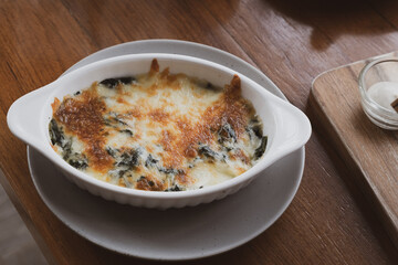 Baked spinach with cheese in a white bowl on the dining table