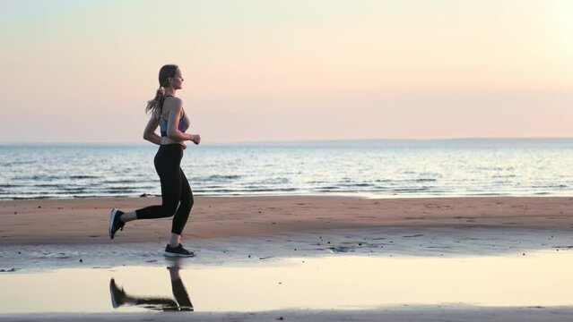 Fitness woman active running jogging cardio training outdoor sunset sand sea beach side view slowmo