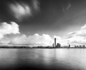 Naklejka premium Morning clouds. Early morning long exposure over Victoria Harbour, Hong Kong with an iPhone and tripod. Coastline with buildings, smooth sea and blurred clouds.