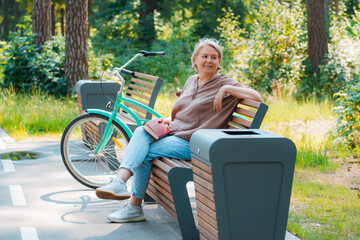 Dreamy modern old lady relaxing in city park. Pensive senior grey haired woman in casual sitting wooden bench outdoors.