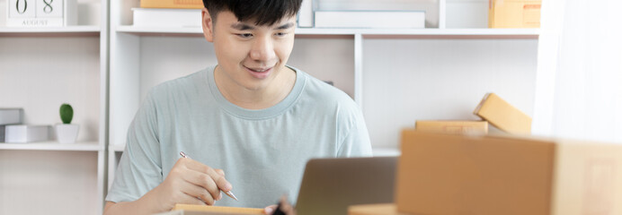 Fototapeta na wymiar Young Asian man is writing down the customer's details and addresses on the notebook or box in order to prepare for shipping according to the information, Packing box, Sell online, freelance working.