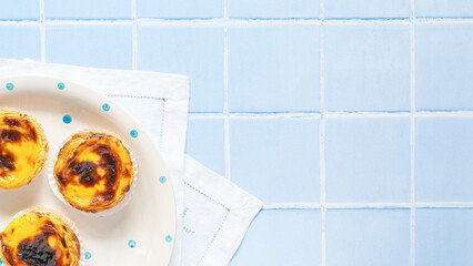 Traditional Portuguese egg tart dessert Pasteis Pastel de nata or Pastels de Belem on the plate on blue tile. Flat lay with copy space