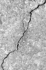 Big diagonal ascending crack on old concrete wall. Vertical black and white photo. Close-up. Copy space. Selective focus.