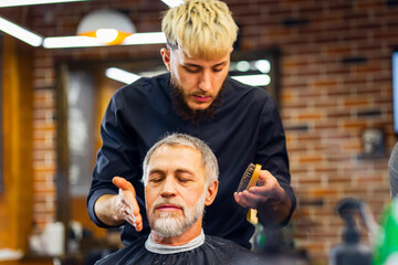 trendy stylish master cuts hair of old man client in modern barbershop