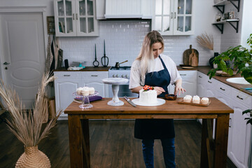 Pastry chef confectioner young caucasian woman with cake on kitchen table. Cakes cupcakes and sweet dessert