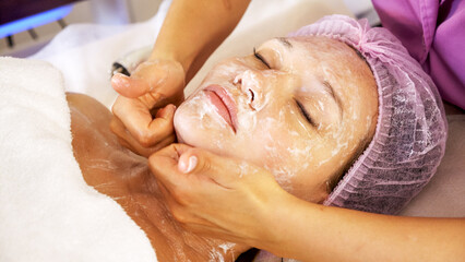 Cosmetologist applies  a moisturizing mask on female face. Woman in a spa salon on cosmetic procedures for facial care.  White woman getting beauty treatment therapy.