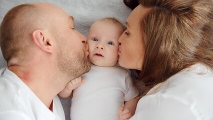 Happy family. Newborn baby with happy parents, top view. Healthy newborn baby in a white t-shirt with mom and dad. Close up Faces of the mother, father and infant baby. Cute Infant boy and parents