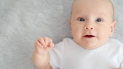 Child's face of a Happy newborn baby looking to camera. Healthy newborn baby in a white t-shirt with blue eyes. Face of a Beautiful active tiny child. Cute white Infant boy, top view.