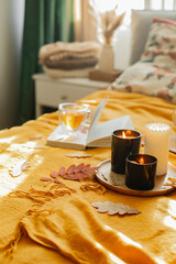 Interior of cozy scandinavian bedroom in autumn colors. Burning candles, cup of tea, open book on bed. Vertical image
