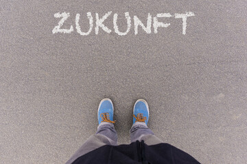 tGerman word Zukunft (future) text on asphalt ground, feet and shoes on floor